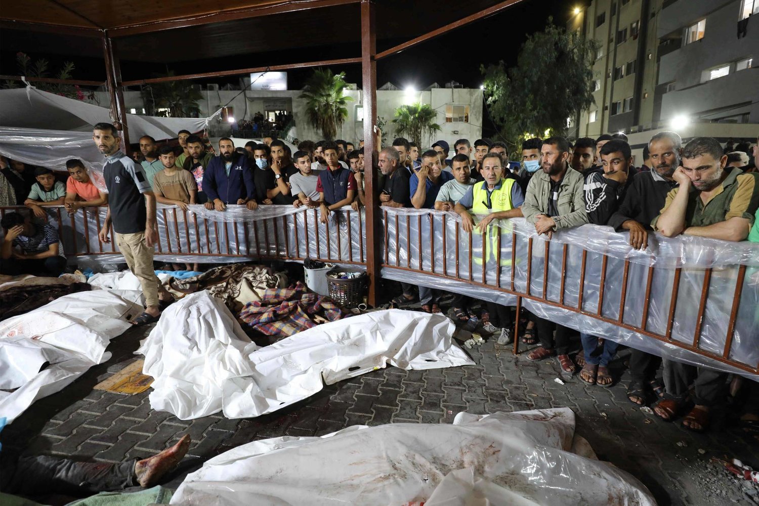 أشخاص يتجمعون حول جثث الفلسطينيين الذين قتلوا في الغارة الجوية الإسرائيلية على المستشفى الأهلي العربي (المعمداني) في وسط غزة بعد نقلهم إلى مستشفى الشفاء في 17 أكتوبر 2023 (أ.ف.ب)